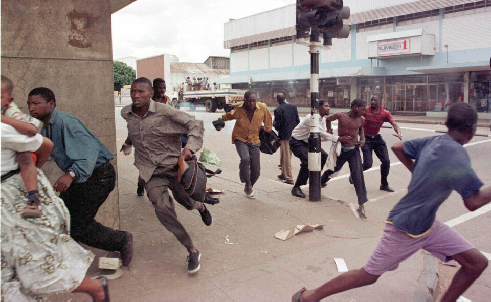 Handlingen i «This Mournable Body» er lagt til sluttten av 1990-årene, et tidspunkt da Zimbabwe langsomt begynte å rakne. Økonomien krasjet og Mugabes styrker slo brutalt ned på all motstand. Her: Demonstranter jages av opprørspoliti etter protester mot økte matpriser, Harare, januar 1998. Foto: Alexander Joe / AFP / NTB